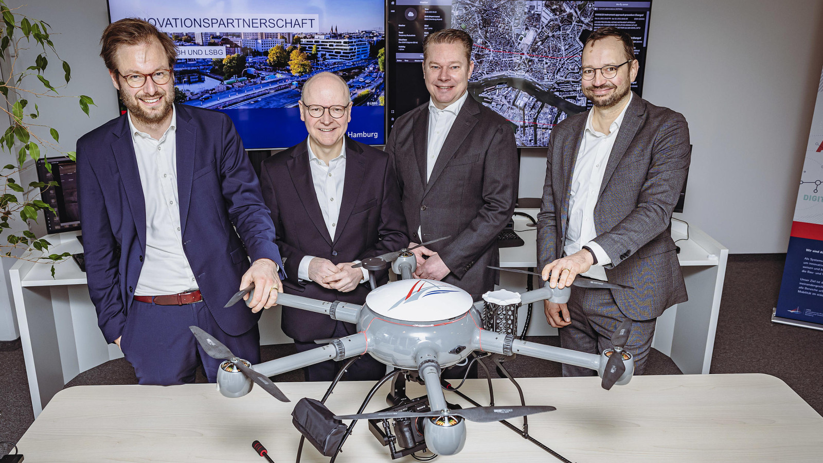 Four men standing behind a drone in office space