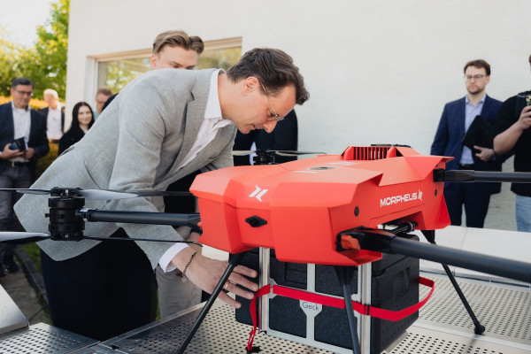 Hendrik Wüst, Minister President of North Rhine-Westphalia, loads a red X25 drone. In the background: Delegation members and representatives from Morpheus Logistik, HHLA Sky and local visitors